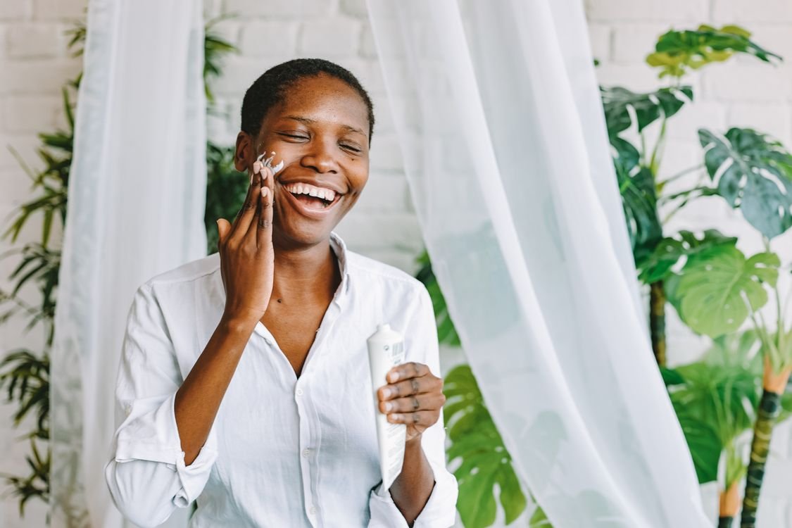 Smiling woman enjoying her skincare routine with face cream in a bright room