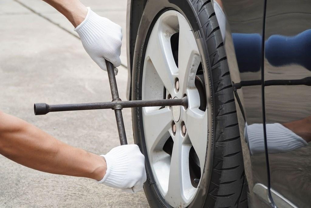Person wearing white gloves using a cross-shaped lug wrench to loosen the lug nuts on a car wheel.