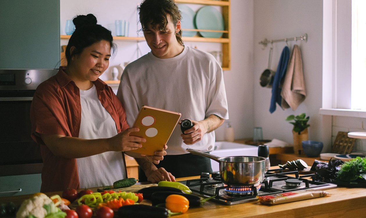 Two people cooking together in a kitchen with fresh vegetables on the counter