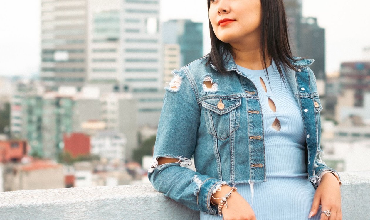 Woman wearing a ripped denim jacket over a light blue dress
