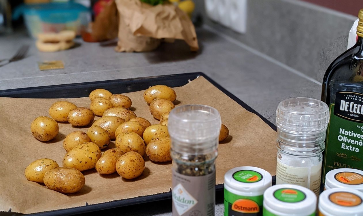 Baking tray of baby potatoes and spice jars on a kitchen counter ready for roasting