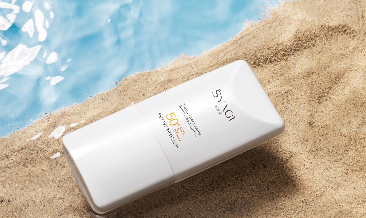 Tube of sunscreen resting on sand beside clear blue water