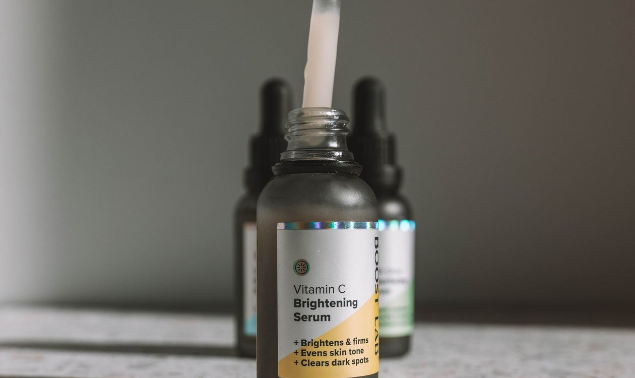 Hand holding a dropper above a vitamin C serum bottle